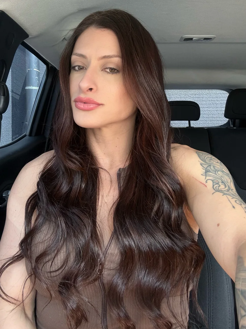 Laura Carnecine em selfie de carro, de cabelo longo, solto e escuro, olhando para a câmera