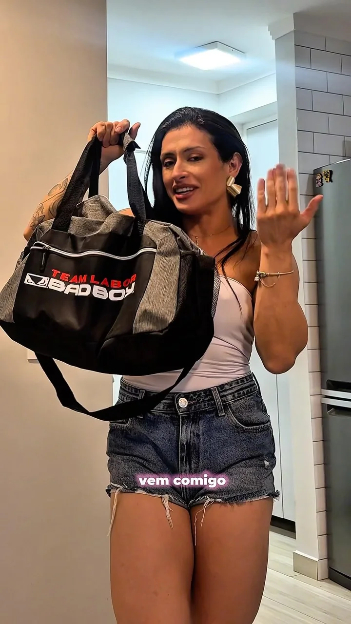 Laura Carnecine segurando uma bolsa de treino BAD BOY, de regata branca e short jeans, com a frase Vem comigo